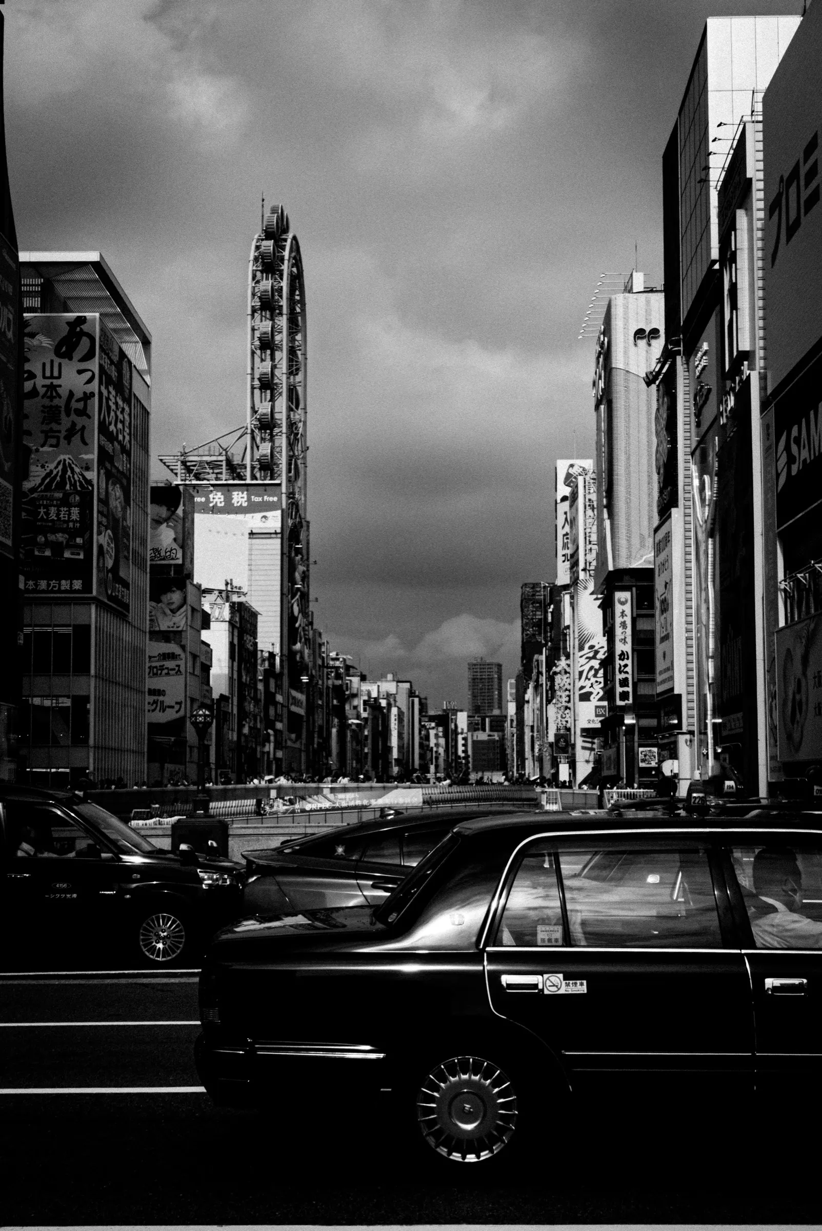 Dark taxis cross a dense city street beneath an overcast sky
