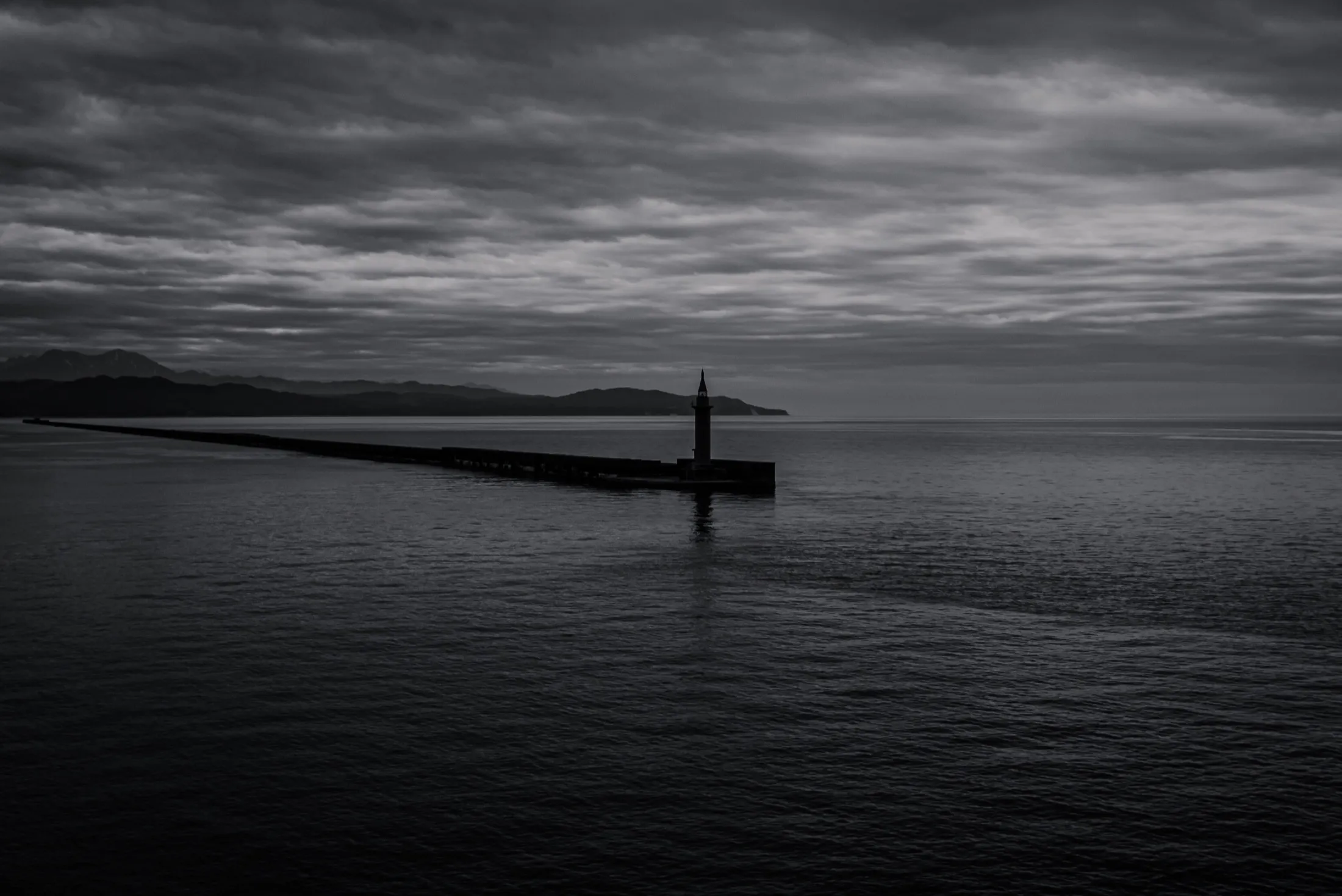 A breakwater lighthouse beneath a long grey sky