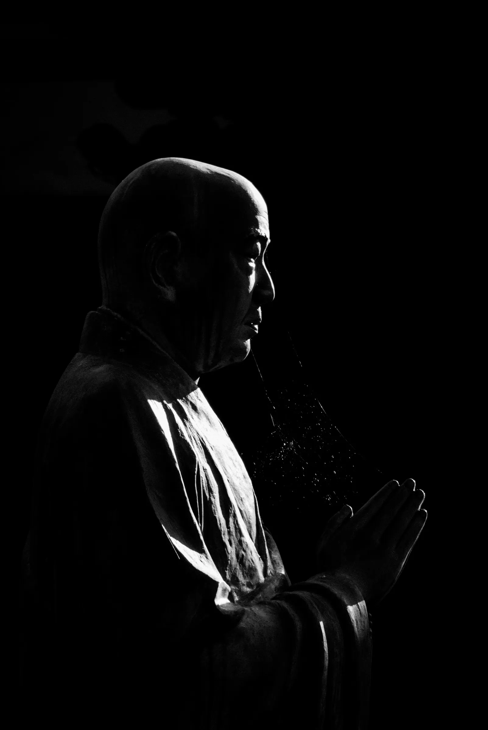 A dark sculpted figure with hands held together in profile