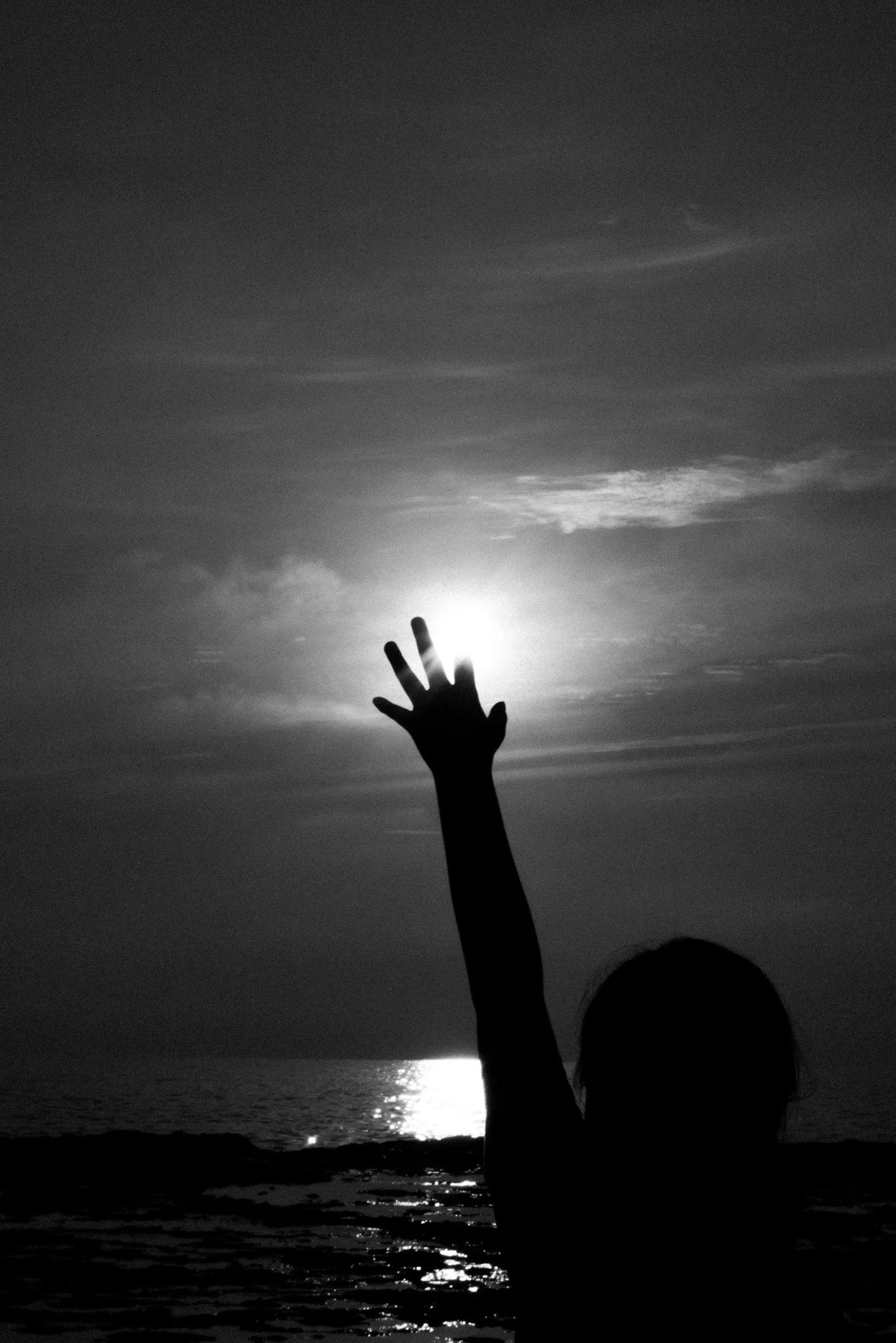 A silhouetted hand reaches toward the sun above the sea