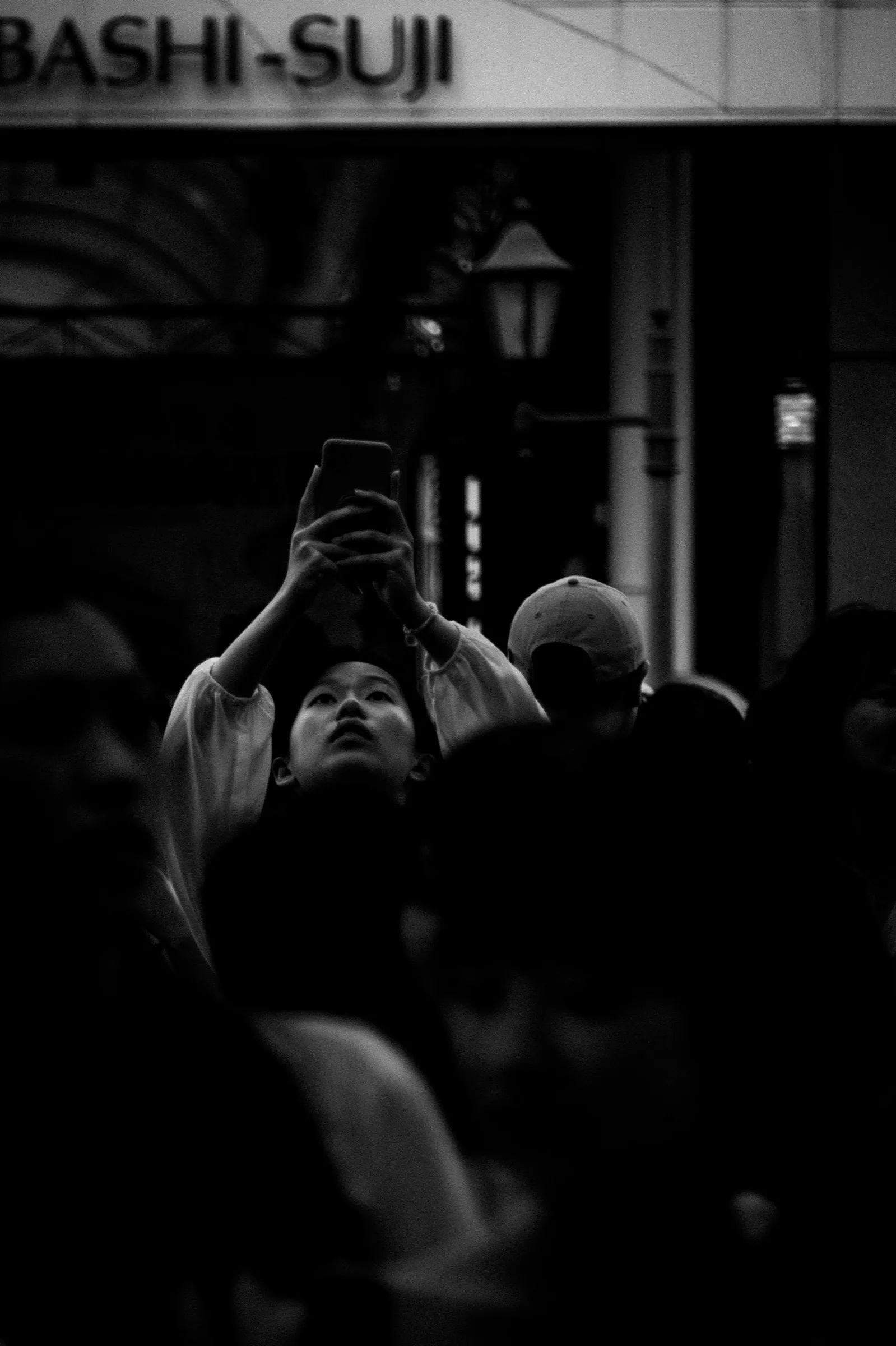A person raises a phone and looks upward inside a crowd