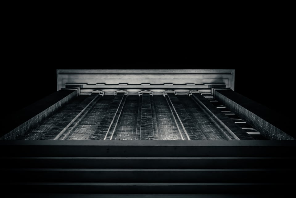 A tall, symmetrical building facade rises out of deep shadow against a black night sky.