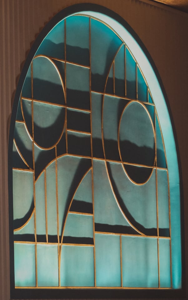 An arched window of teal and gold stained glass.