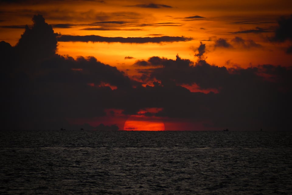 The sun sets into the horizon under stacked orange cloud.