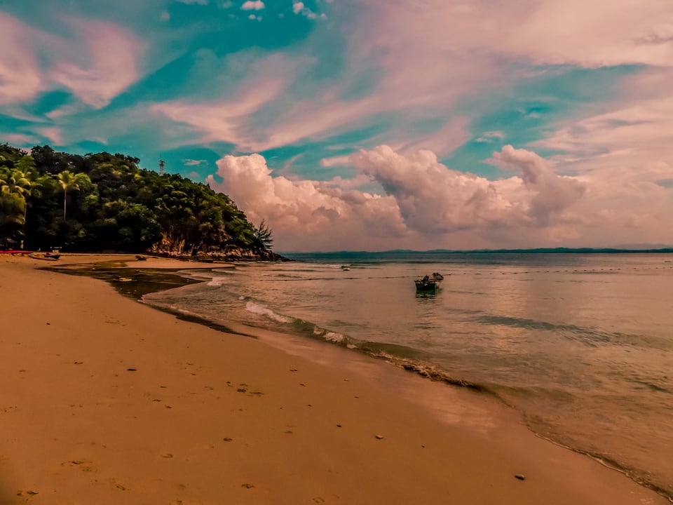 A curve of sand runs to a wooded headland under bright cloud.