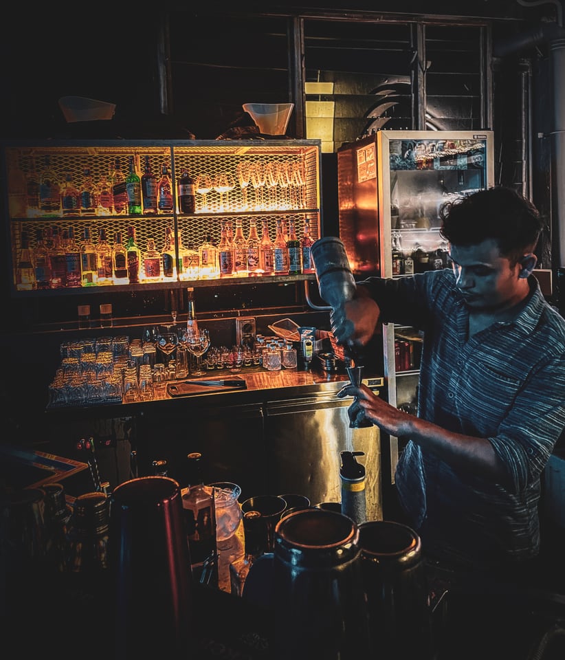 A bartender works behind a lit bar of bottles and glasses.