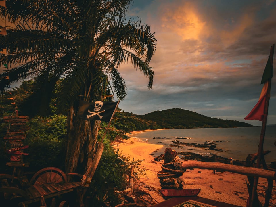 A pirate flag flies over a beach bar at sunset.