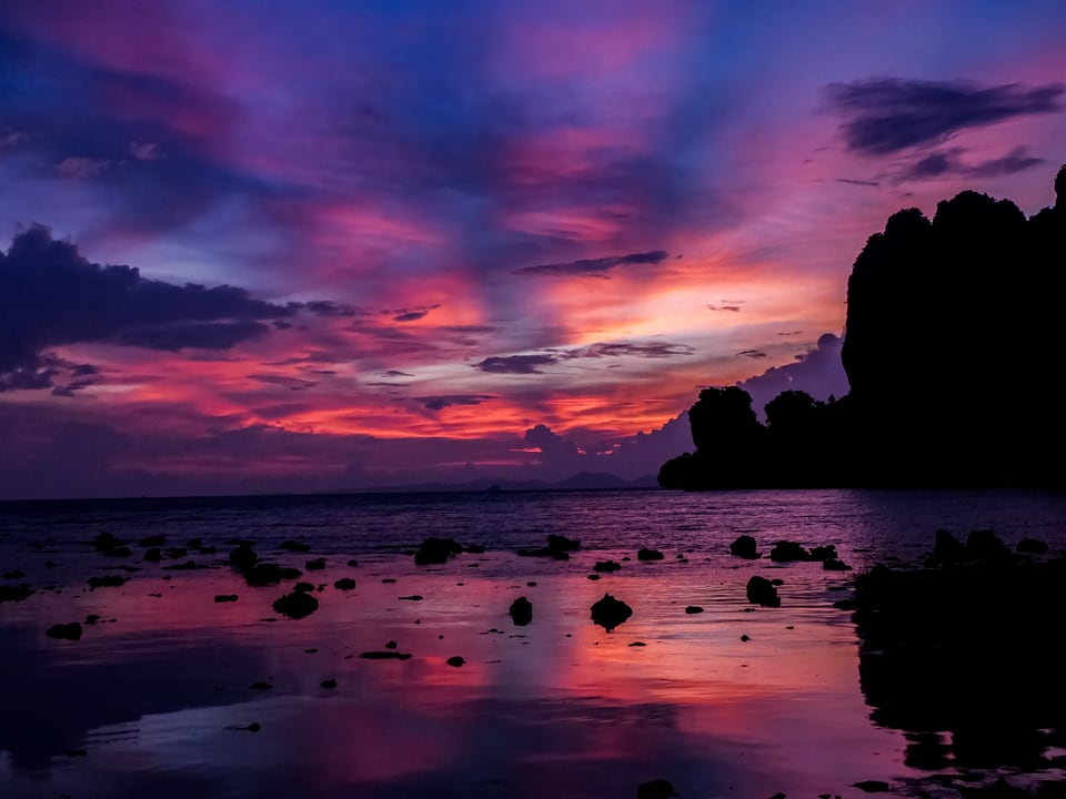 Violet and pink cloud reflects in rock-strewn shallows at dusk.