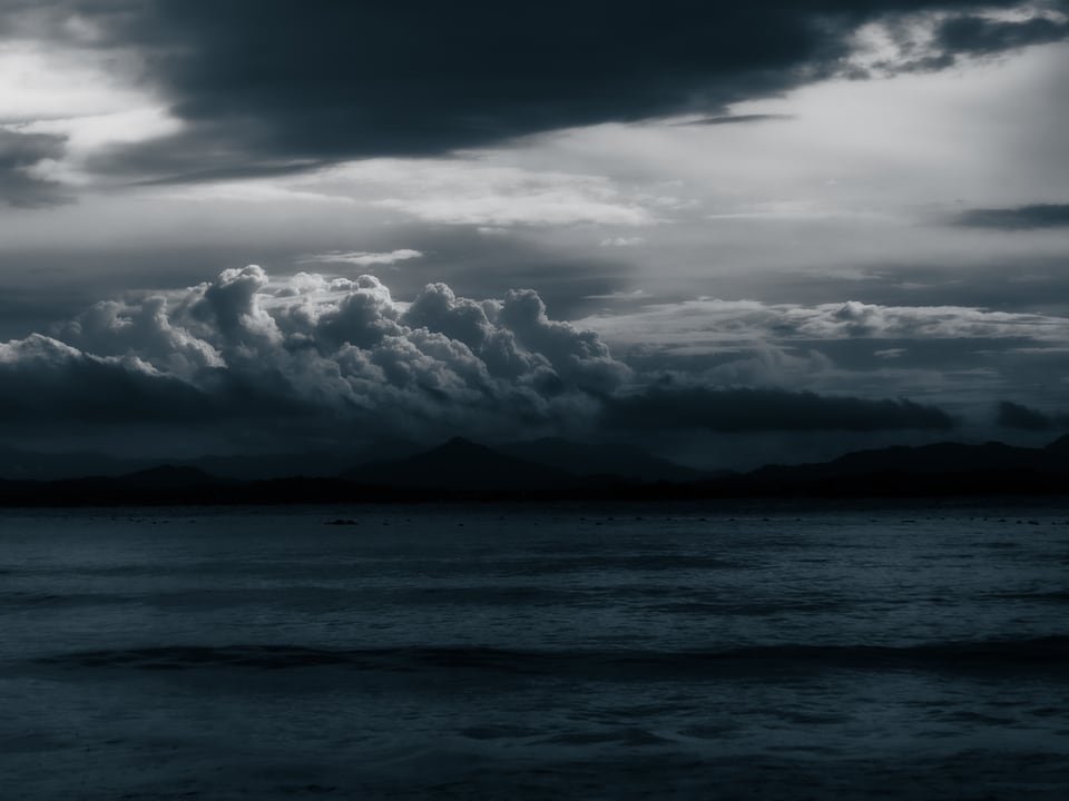 Storm cloud hangs low over a dark sea and distant hills.