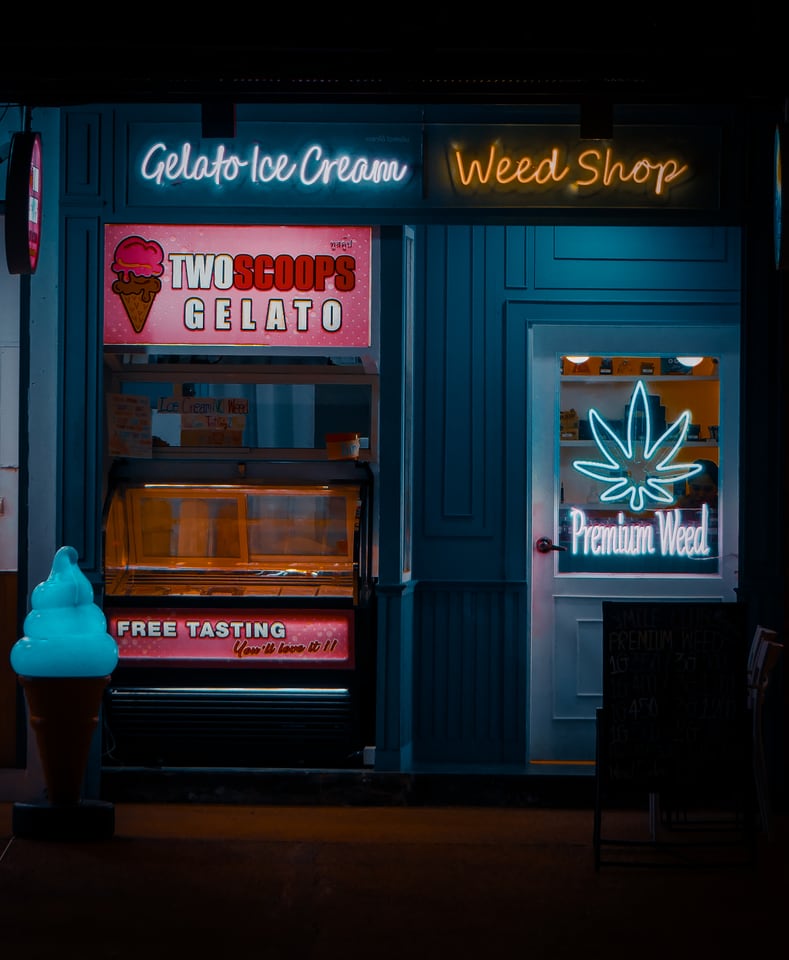 A brightly lit shopfront at night advertising gelato beside a neon cannabis-leaf sign.