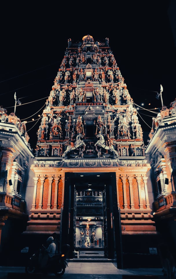A carved and lit temple tower rises above its doorway at night.