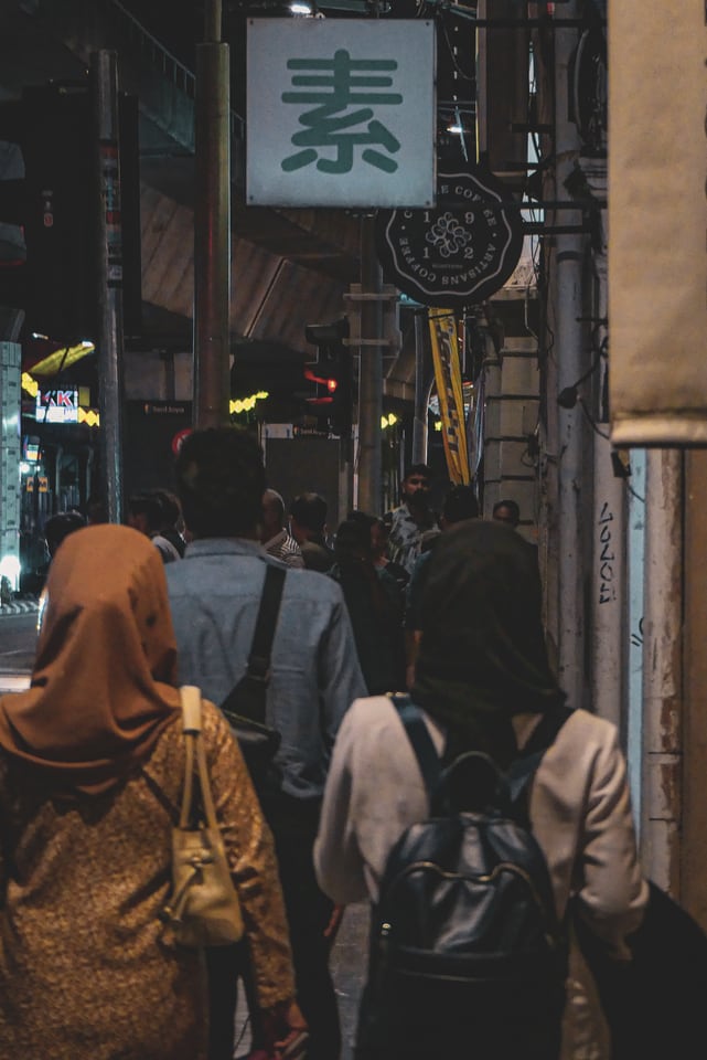 People walk away down a narrow street below a hanging sign.
