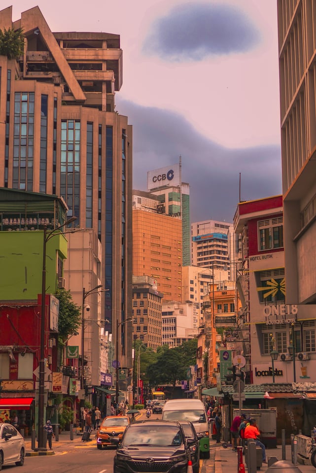 A busy street of shophouses and signage, traffic below and office towers standing behind.
