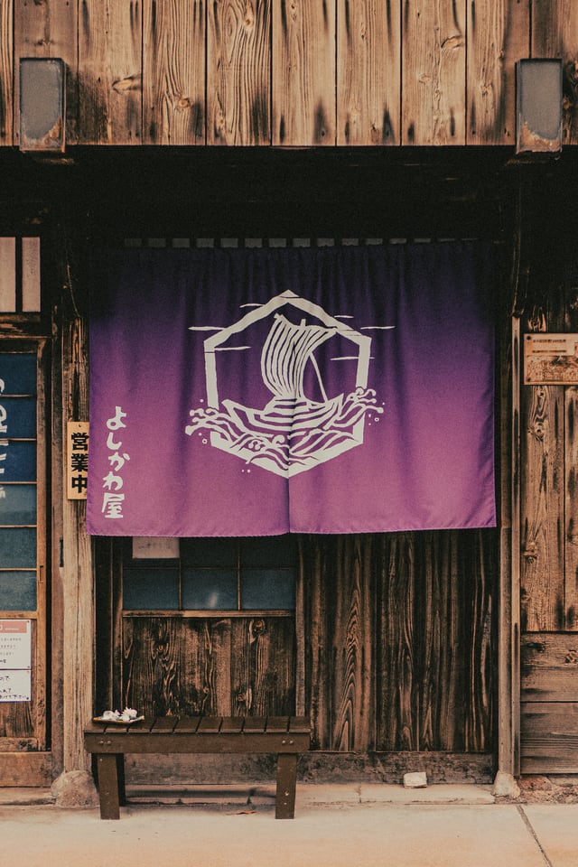 A purple cloth curtain printed with a sailing-ship emblem hangs across the entrance of a weathered timber building.