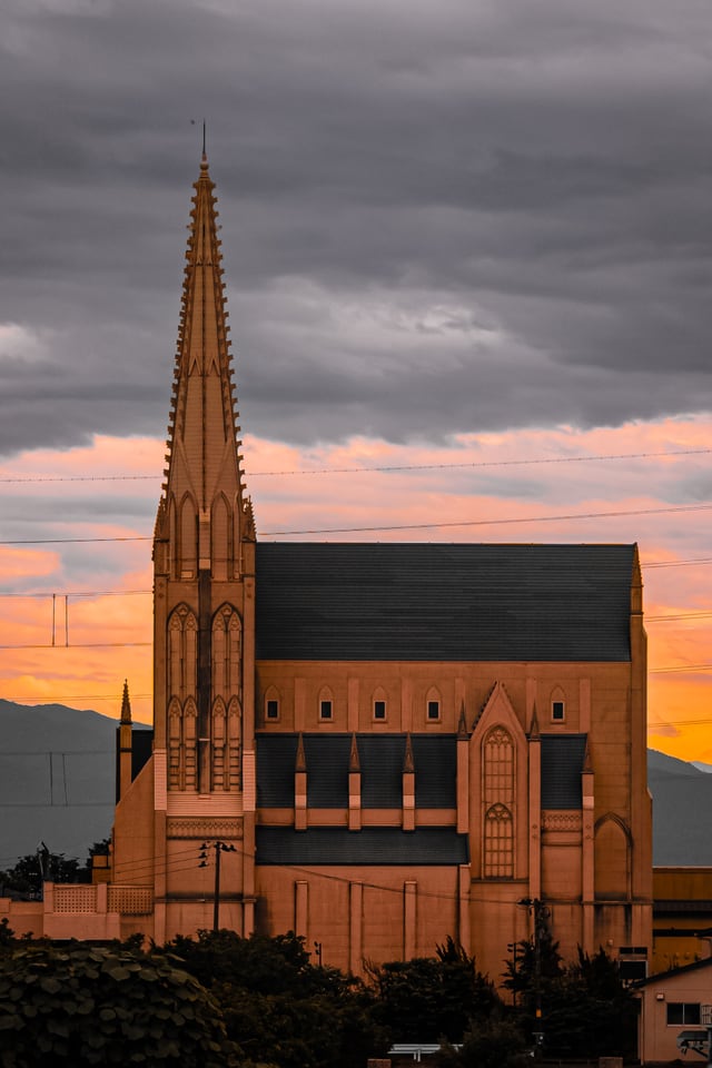 A brick church with a tall spire stands against an orange evening sky.