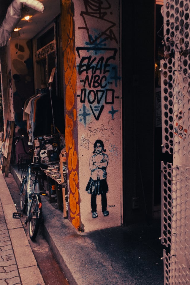A cyclist passes a wall of stickers and spray paint in a narrow lane.