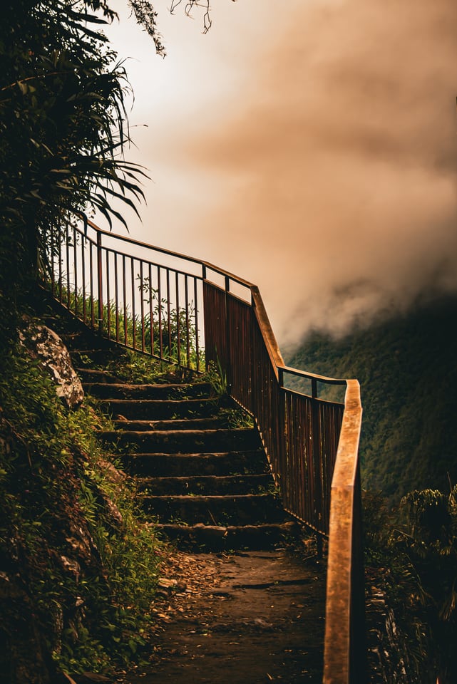 A stone stairway with a wooden rail climbs into rising mist.