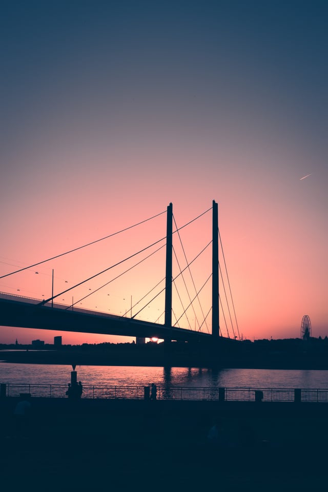 A cable-stayed bridge crosses the river under a pink evening sky.