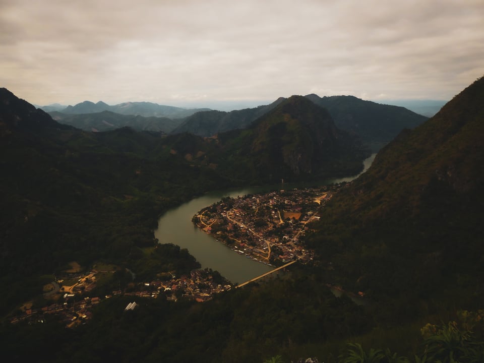 The river curves around Nong Khiaw beneath steep, densely wooded mountains.