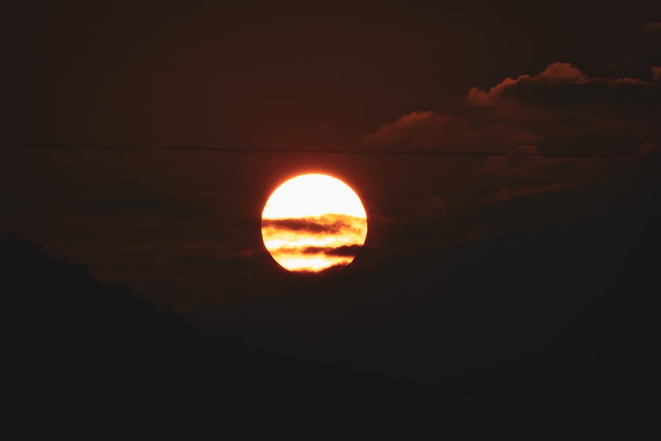 The sun sits low and clear above a dark ridge.