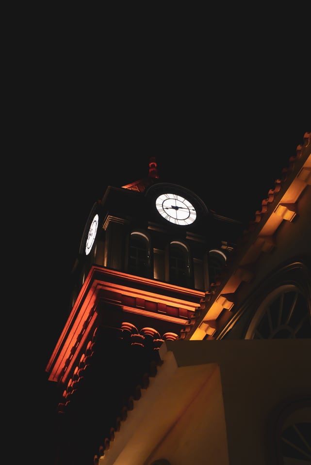 A clock tower glows orange against the dark night sky, seen at a steep angle from below.