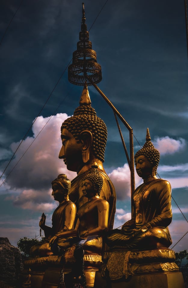 Four gilded seated Buddha figures in profile against a dark blue sky and a bank of cloud lit pink.